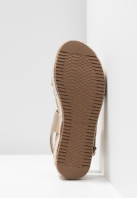 Semelle de sandale avec motif de bande de roulement en caoutchouc marron texturé, logo "Call It Spring" embossé, sangle beige visible sur le côté, sur fond blanc d'angle.