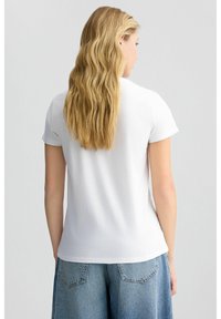 T-shirt en coton blanc avec un col rond et des manches courtes, présentant une texture lisse et une coupe décontractée, associé à un short en denim bleu clair.