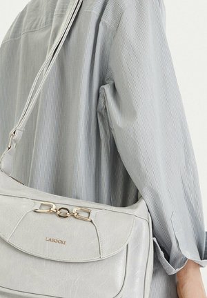 Bolso de hombro de cuero gris claro con detalle de cadena dorada, llevado sobre el brazo con una camisa de manga larga a rayas finas, sobre fondo blanco.