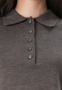 Polo shirt en tricot marron avec un col, cinq boutons à l'avant et une texture lisse. Le tissu semble doux et bien ajusté autour du cou.