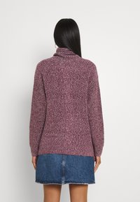 Burgundy neulepaita korkealla kauluksessa, jossa on tekstuuri ja pitkät hihat, yhdistettynä farkkuhameeseen.