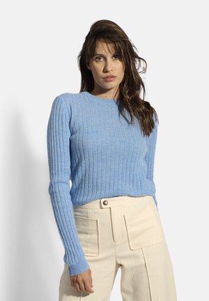 Maglione a coste blu cielo con maniche lunghe e scollatura rotonda, abbinato a pantaloni color crema con tasche frontali e dettaglio dei bottoni.
