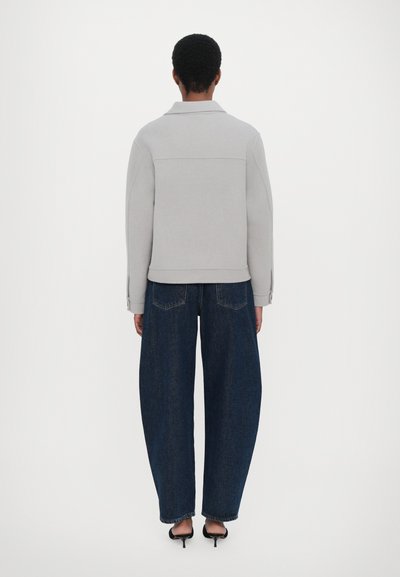 Gray sweatshirt with a structured collar, paired with loose-fitting dark blue jeans. Model wearing black heeled sandals.