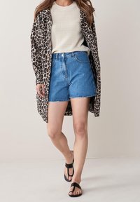 Løveprint lang skjortejakke parret med en cremefarvet strikket top og højtaljede blå denimshorts. Sorte strop sandaler fuldender looket.