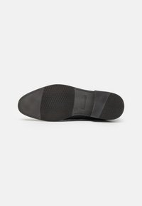 Semelle de sneaker noire présentant un design en caoutchouc texturé, avec une partie avant lisse et un motif de grip à la surface inférieure pour une traction optimale.