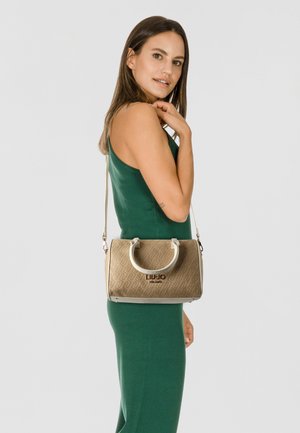 Sac à main à motif doré avec éléments blancs, forme structurée, poignées supérieures et bandoulière réglable, présenté sur un fond neutre.