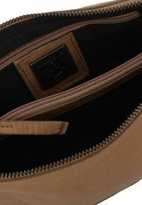 Borsa con zip in pelle marrone chiaro con fodera in tessuto nera. Presenta una superficie liscia, una piccola linguetta in pelle e un'etichetta metallica con il marchio.