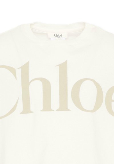 Biały top z okrągłym dekoltem z dużym beżowym napisem „Chloé” na piersi i małą etykietą marki przy dekolcie.