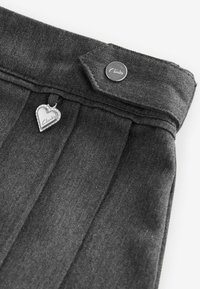 Denim grigio scuro con pieghe, dotato di un bottone argentato e di un'etichetta metallica a forma di cuore incisa con la scritta "Clarks". Dettaglio del tessuto testurizzato visibile.