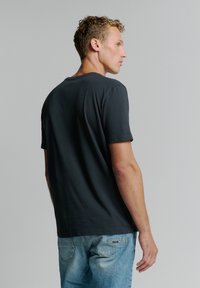 Zwarte katoenen T-shirt met een eenvoudige ronde hals en korte mouwen, gedragen met lichtblauwe jeans, van achter bekeken.