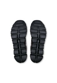 Semelles de chaussures de sport noires avec un motif de grip texturé, design segmenté pour la flexibilité, et détail de marque visible près du centre.