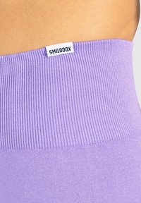 Fioletowe legginsy z wysokim stanem, z ribbowanym pasem, z białą metką "SMILODOX". Gładka tekstura i dopasowany krój.
