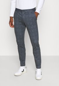 Gray checkered trousers with a tailored fit, featuring a button closure and side pockets, paired with white sneakers.