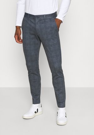 Pantaloni a quadretti grigi con vestibilità sartoriale, dotati di chiusura con bottone e tasche laterali, abbinati a sneaker bianche.