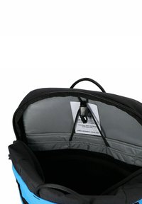 Interno dello zaino che mostra una fodera imbottita grigia, un cordino bungee nero regolabile e l'etichetta del marchio cucita all'interno del flap superiore.