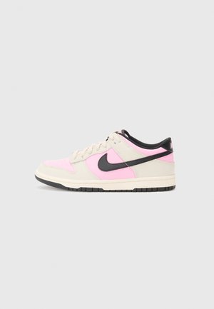 Sneakers Nike Dunk, z beżowo-różową skórzaną cholewką, czarnym Swooshem, teksturowaną powierzchnią i ciemną gumową podeszwą.