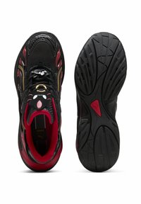 Černé sportovní boty s červenými akcenty, texturované černé a zlaté detaily, zaoblený design a gumová podešev s profilovým vzorem.