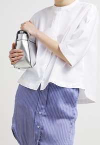 Vit kortärmad skjorta i kombination med en blårandig kjol. Personen håller en liten, silverfärgad metallväska med en stilren, modern design.