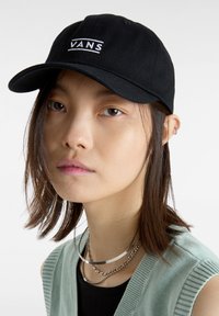 Gorra negra con el logo bordado de "VANS", material de algodón, visera curvada, correa ajustable, llevada en un ángulo ligero en la cabeza de una persona.