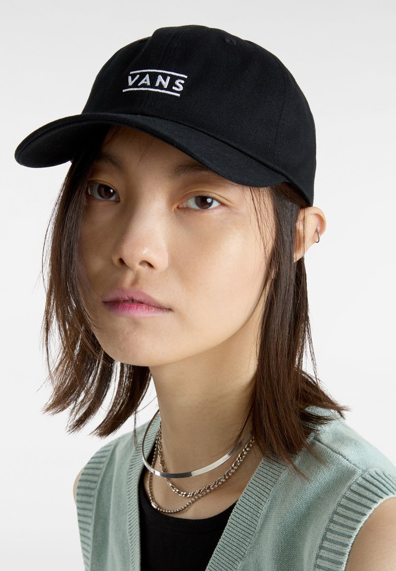 Gorra negra con el logo bordado de "VANS", material de algodón, visera curvada, correa ajustable, llevada en un ángulo ligero en la cabeza de una persona.