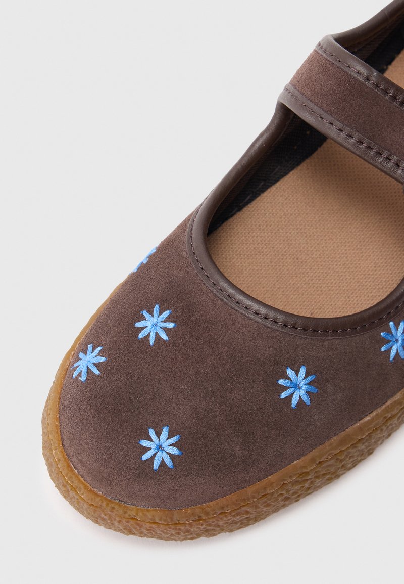 Brown suede shoe with a rounded toe, decorated with blue flower embroidery, featuring a brown elastic strap and a textured rubber sole.