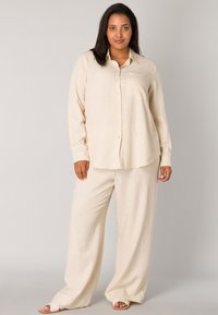 Beige long-sleeve button-up shirt with a pocket, paired with wide-leg pants in matching color. Soft, lightweight fabric, relaxed fit.