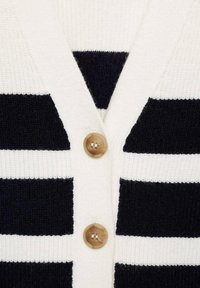 Cardigan a righe con strisce verticali bianche e nere, realizzato in tessuto texturizzato. Presenta un collo a V e due bottoni in legno sulla parte anteriore.