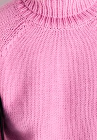 Rosa stickad tröja med hög halsringning, ribbad krage och mjuk textur. närbild av tyget med en slät yta.