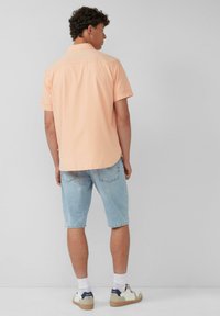 Korte mouwen, perzikkleurig overhemd met een kraag, gecombineerd met lichtblauwe spijkerbroek-shorts en witte sneakers met accenten. Achteraanzicht zichtbaar.