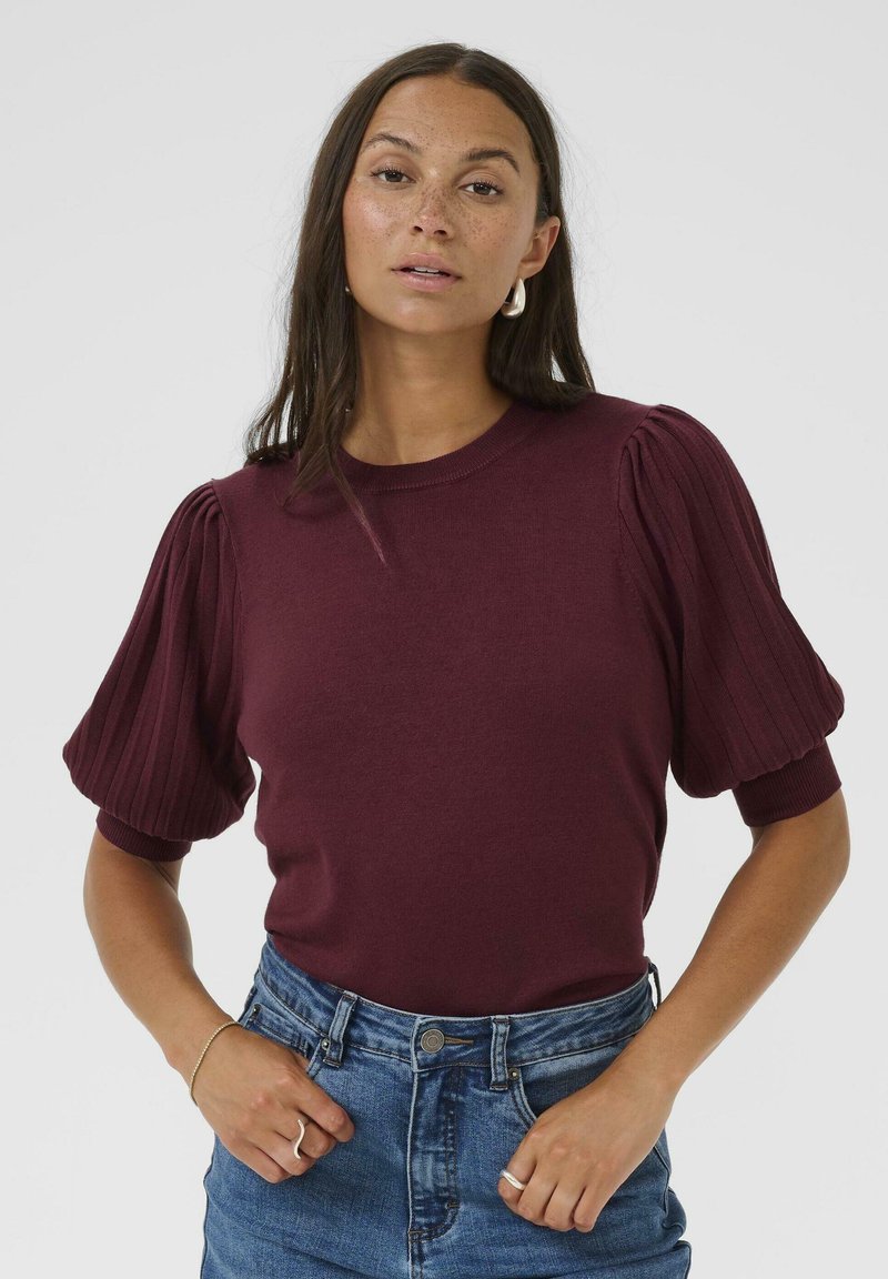 Burgundy tröja med ribbade, puffiga korta ärmar. Mjuk textur och rund halsringning, tillsammans med högmidjade denimshorts.