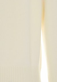 Maglione a maglia color crema con orlo a coste, caratterizzato da una texture liscia e un design senza cuciture; la luce filtra attraverso il tessuto.