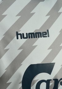 Gros plan d'un tissu blanc avec un motif d'éclair gris clair et un texte noir "hummel" au-dessus d'une partie d'une grande lettre noire.