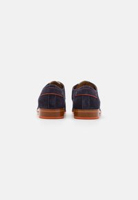 Scarpe in suede blu navy con cuciture e dettagli rossi a contrasto, caratterizzate da una suola in legno marrone e un tacco arrotondato.