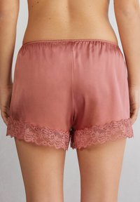 Satinrosa shorts med mjuk spetsdetalj i fållen, med resårmidja för komfort och en slät textur.