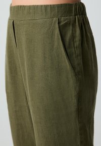 Olivgrüne Hose aus strukturiertem Stoff, mit elastischem Bund und vorderen Falten. Verfügt über seitliche Taschen und ein gerades Bein.