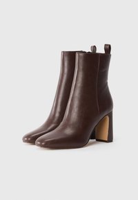 Brown leather ankle boots with a pointed toe, structured design, and a block heel. Features a loop tab for easy wear.