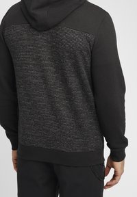 Sudadera con capucha negra que presenta un respaldo texturizado con finas rayas horizontales en un tono más claro. Puños y dobladillo acanalados; acabado de tela suave.
