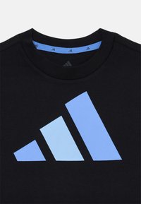 Svart bomull T-skjorte med en stor lyseblå Adidas-logo som har tre diagonale striper. Utringningen har en kontrastfarge i lyseblått.