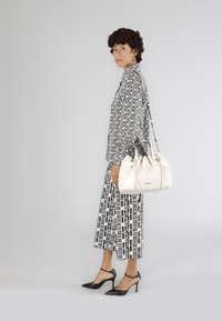 Borsa a tracolla bianca in pelle con un design arricciato e hardware silver. Indossata con un outfit a motivo geometrico bianco e nero e tacchi neri.