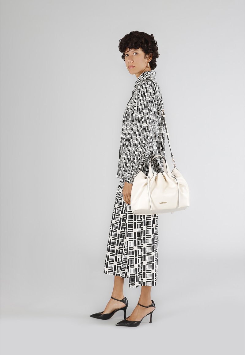 Borsa a tracolla bianca in pelle con un design arricciato e hardware silver. Indossata con un outfit a motivo geometrico bianco e nero e tacchi neri.