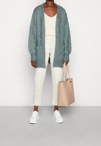 Lichtblauwe gebreide cardigan met open voorkant, crèmekleurig tanktop, witte cropped broek, witte sneakers en een beige schoudertas.