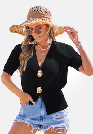 Czarny dziany kardigan z krótkimi rękawami, ozdobiony trzema złotymi guzikami w kształcie kwiatów; noszony z postrzępionymi krótkimi dżinsami i dodatkami.