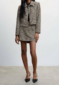 Set di giacca tweed e mini gonna in tessuto check beige, nero e crema. Giacca corta, gonna slim fit, abbinata a tacchi neri a punta.