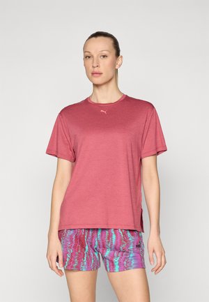 Camiseta roja de manga corta con cuello redondo y ligeras aberturas laterales, combinada con pantalones cortos de patrón púrpura y azul que presentan un logo.