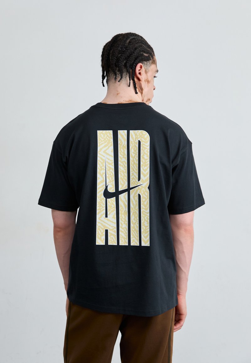 Black t-shirt featuring large "AIR" graphic in textured gold on the back; relaxed fit with short sleeves, round neckline.