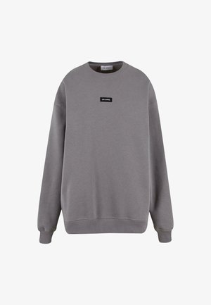 Pelēks krekls ar mīkstu audumu, ar apaļu kaklu, garām piedurknēm un mazu melnu etiķeti ar uzrakstu "OH APRIL" priekšā.