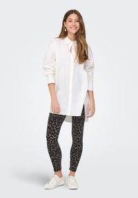 Witte blouse met lange mouwen, gecombineerd met zwarte leggings met panterprint en witte sneakers. Glad stof en een ontspannen pasvorm.