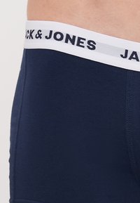 Marineblaue Boxershorts aus Baumwolle mit einem weißen elastischen Bund, auf dem "JACK & JONES" in dunklen Buchstaben gedruckt ist. Glatte Textur und taillierte Passform.