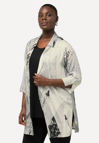 Camicia colletto, con bottoni, di colore bianco e grigio con motivi astratti neri; presenta maniche a tre quarti e spacco laterale per una vestibilità rilassata.