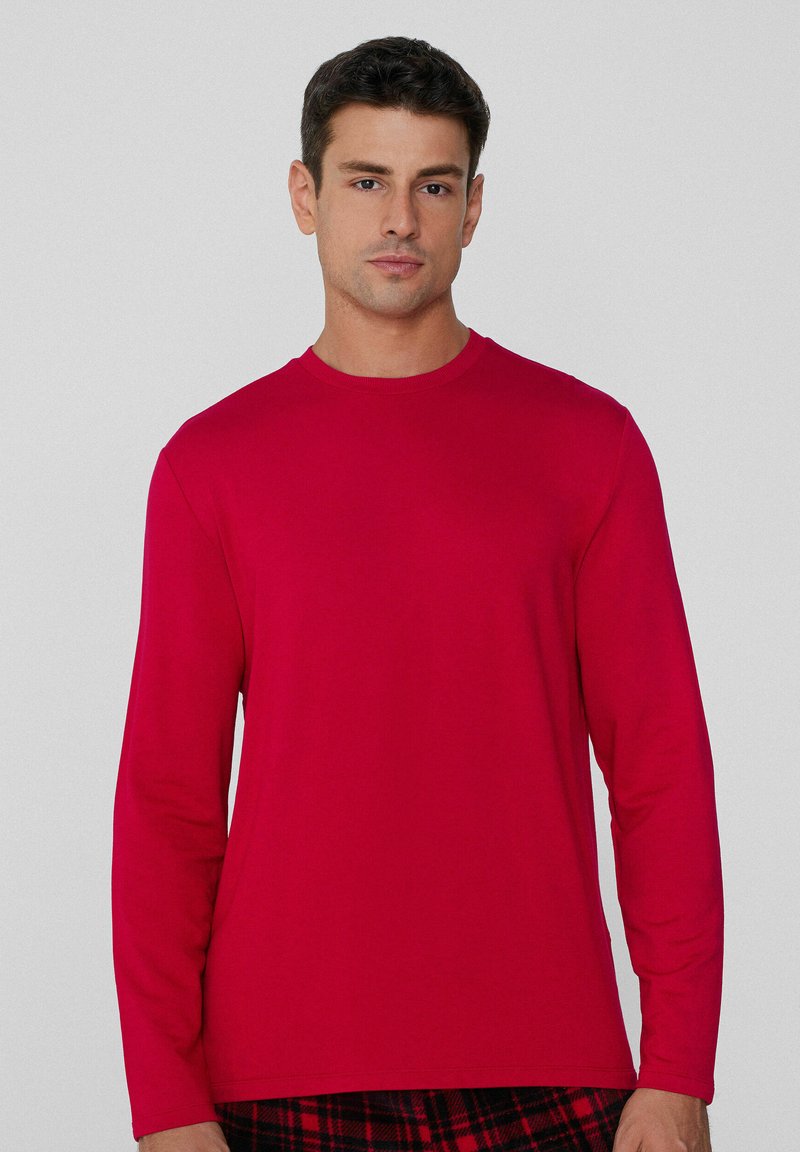 Camiseta roja de manga larga hecha de tela suave, con cuello redondo y un diseño ajustado, llevada sobre pantalones de cuadros en negro y rojo.
